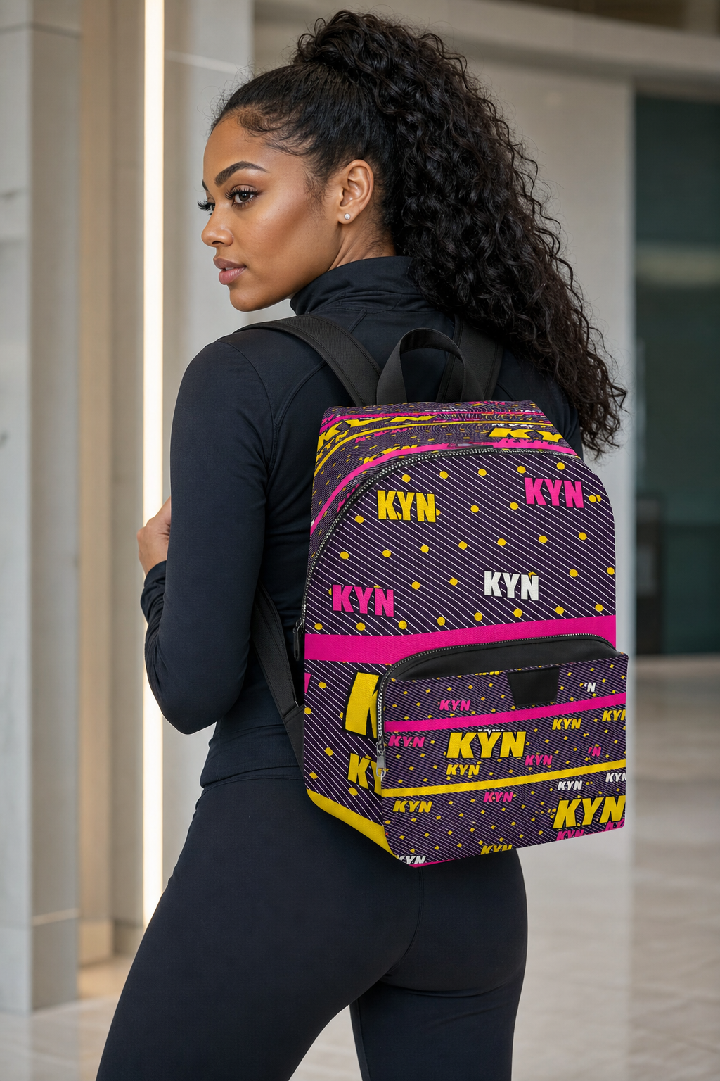 Woman wearing a backpack with 'KYN' pattern in an indoor setting