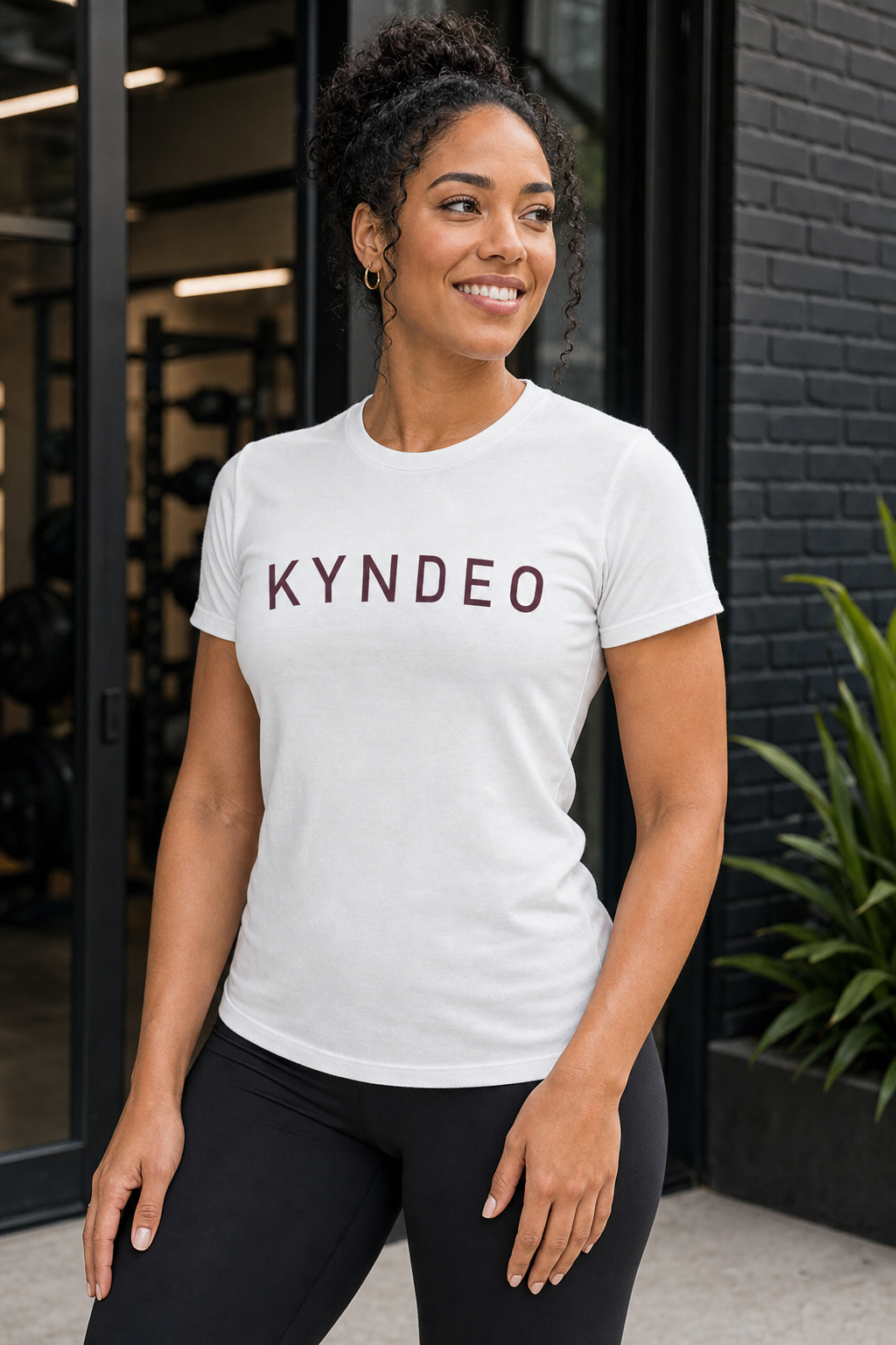 Woman wearing a white t-shirt with 'KYNDEO' printed on it, standing outdoors.