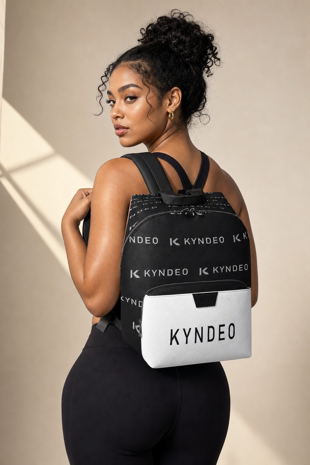 Woman wearing a black backpack with 'KYNDEO' branding on a beige background