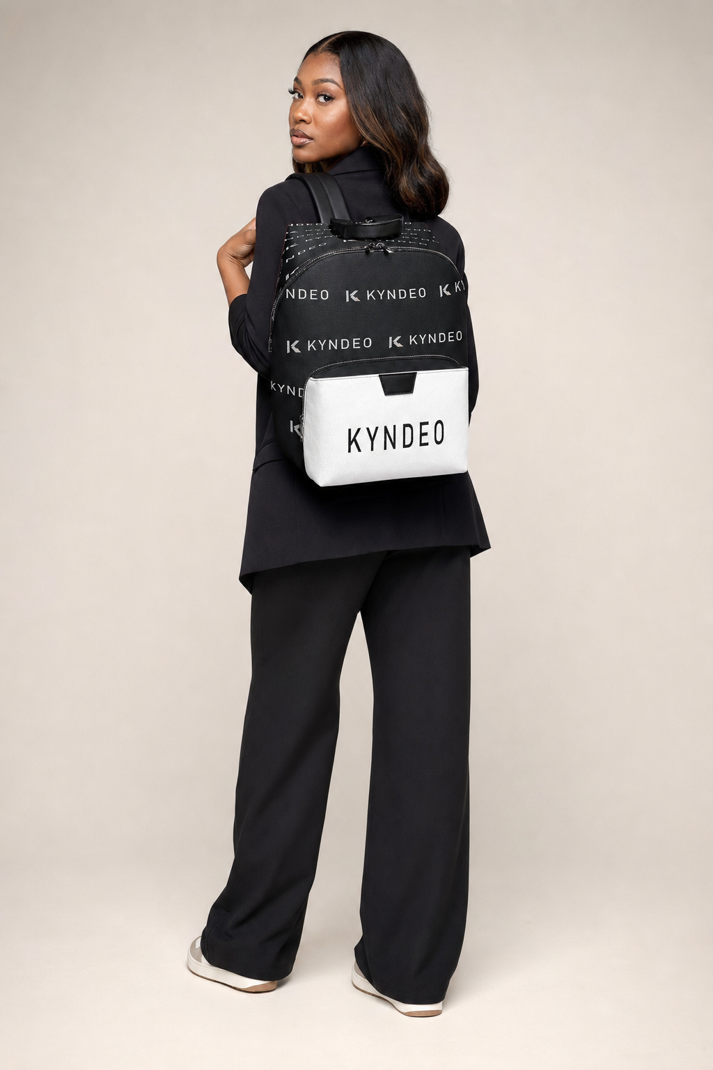 Person holding a black and white bag with 'KYNEDE' branding against a beige background
