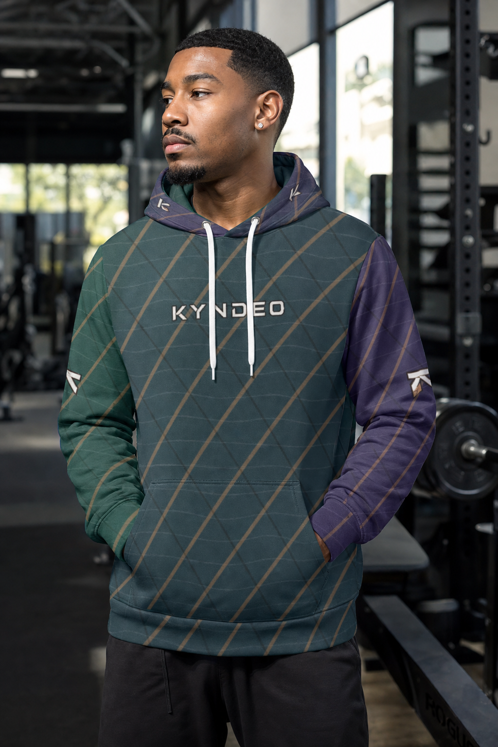 Man wearing a green and purple striped hoodie with 'KYNEDE' branding in a gym setting
