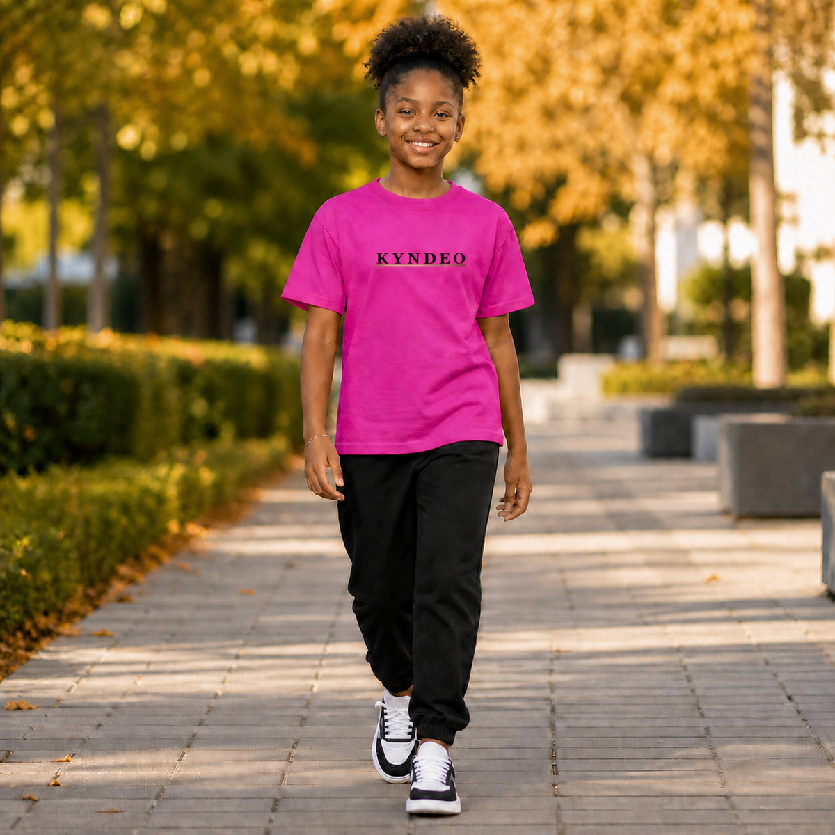 KYNDEO Youth Pop Tee on a Black girl model walking through an autumn park