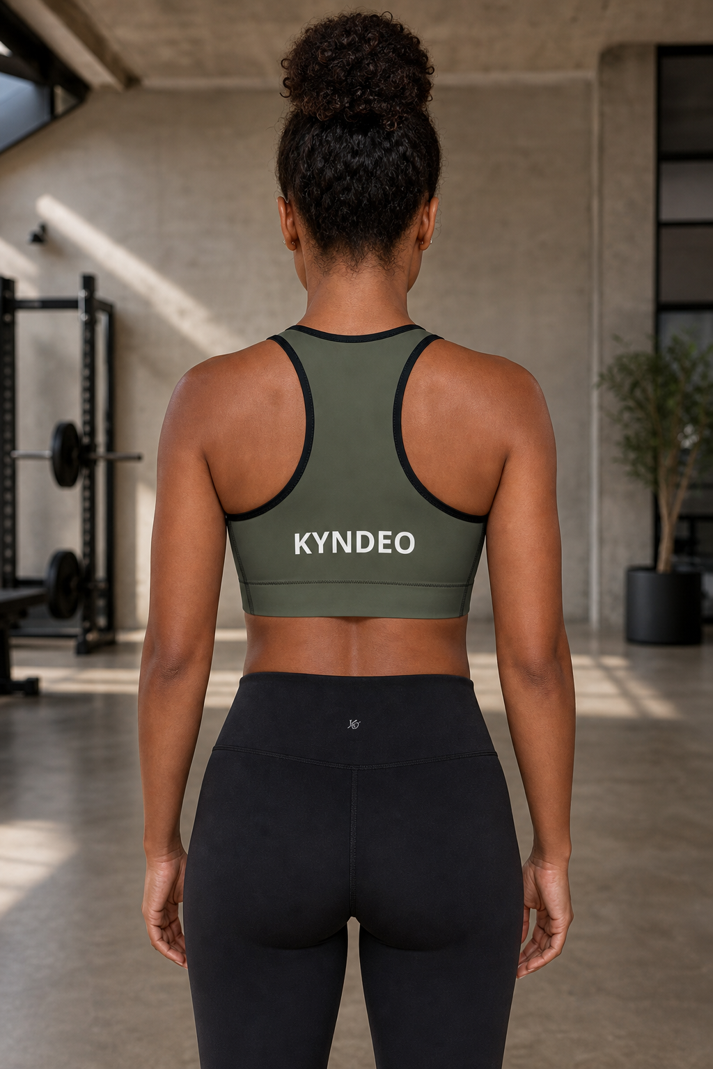 Afro-Latina woman showing the olive KYNDEO Shadow Form Sports Bra racerback, straight back view