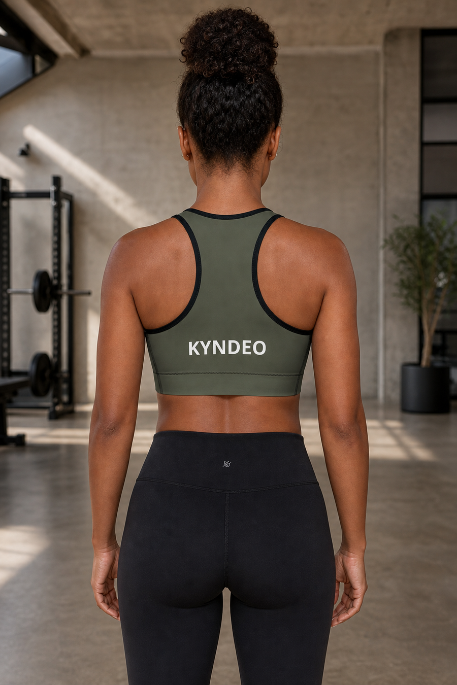 Afro-Latina woman showing the olive KYNDEO Shadow Form Sports Bra racerback, straight back view